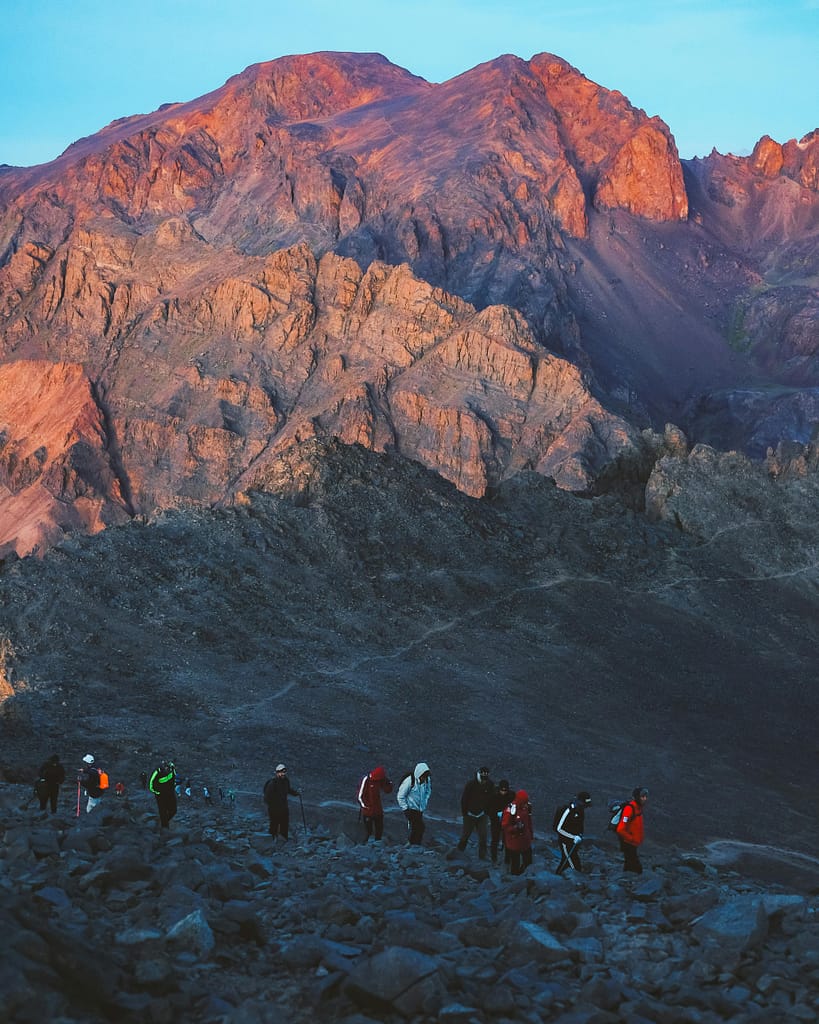 A group of hikers walking through rocky terrain in the scenic Al-Aroui mountains at dusk.